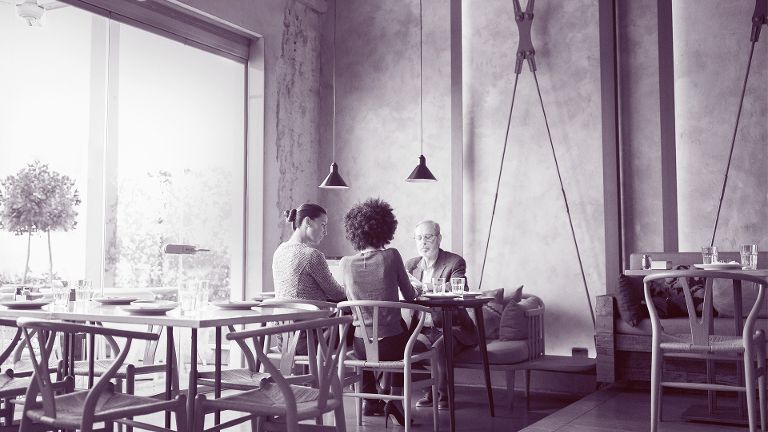 Zwei Frauen und ein älterer Mann sitzen in einem Café an einem Tisch im Innenraum