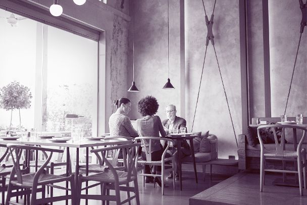Zwei Frauen und ein älterer Mann sitzen in einem Café an einem Tisch im Innenraum